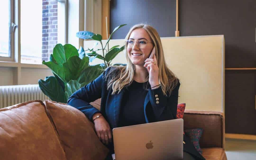 woman with laptop on her lap and holding a phone in office