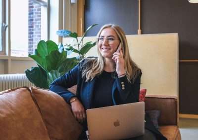 woman with laptop on her lap and holding a phone in office