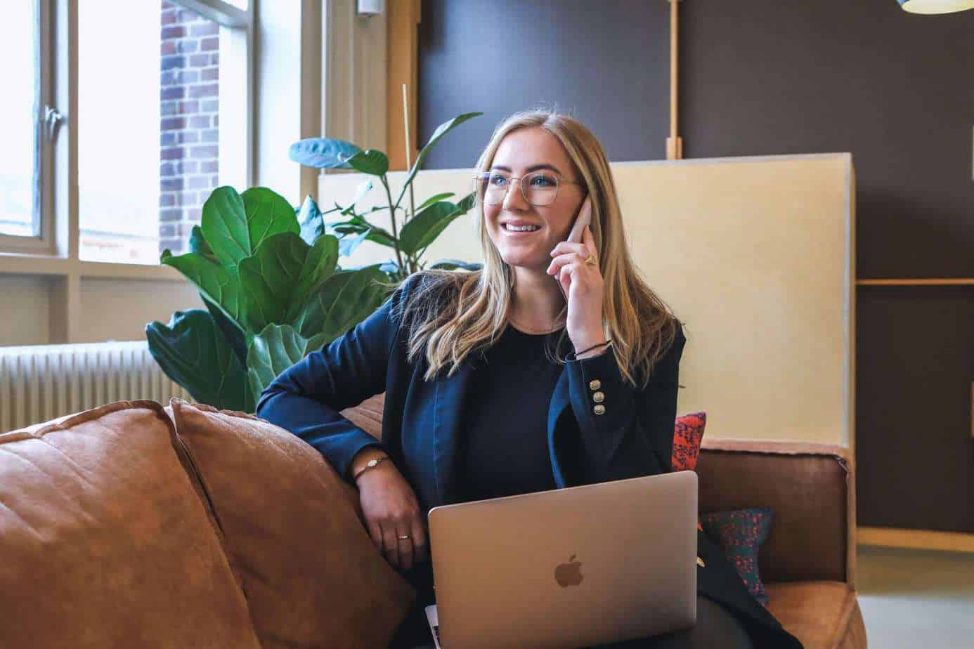 woman with laptop on her lap and holding a phone in office