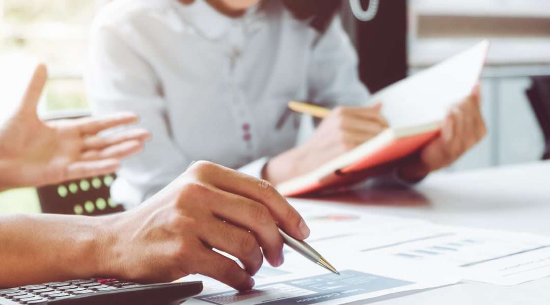 Two people sitting at a desk with calculators and looking at graphs and charts.