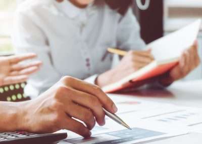 Two people sitting at a desk with calculators and looking at graphs and charts.