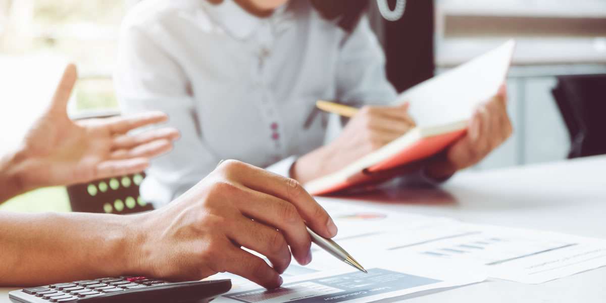 Two people sitting at a desk with calculators and looking at graphs and charts.