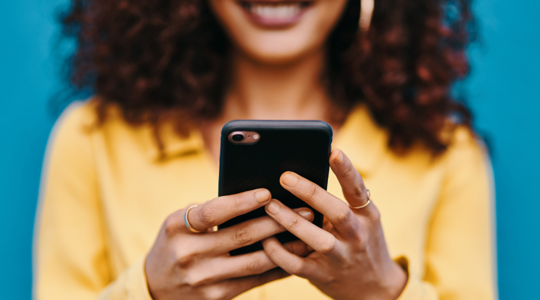 Closeup of woman in a yellow shirt holding a black cell phone.