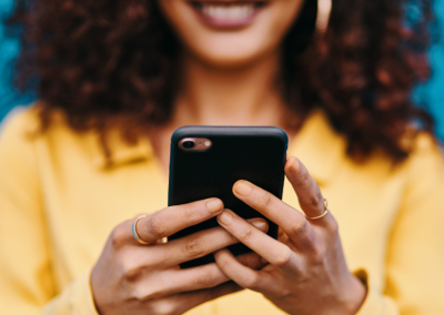 Closeup of woman in a yellow shirt holding a black cell phone.