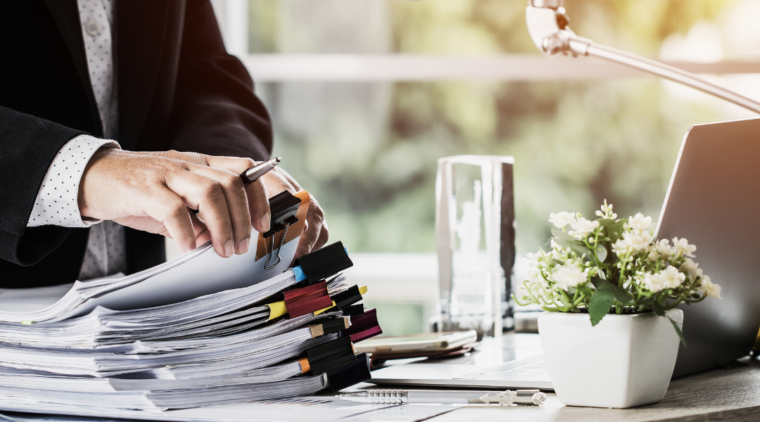 Close-up of a man sifting through a large stack of papers, binder-clipped into different stacks.