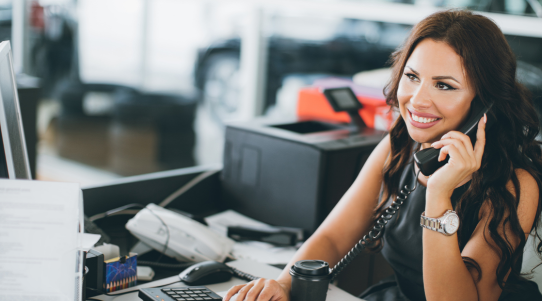 A woman smiling at her desk while holding a phone to her ear.