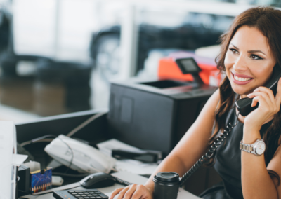 A woman smiling at her desk while holding a phone to her ear.