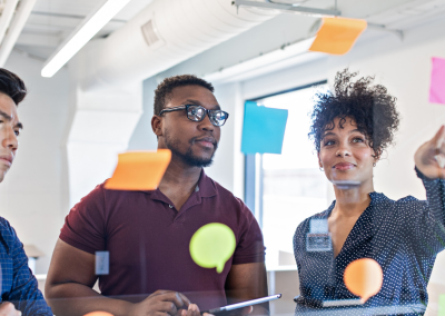 A woman and two men looking at a clear board covered with brightly colored sticky notes.