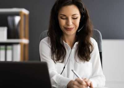 A woman in a black office wearing a headset and working at a laptop.