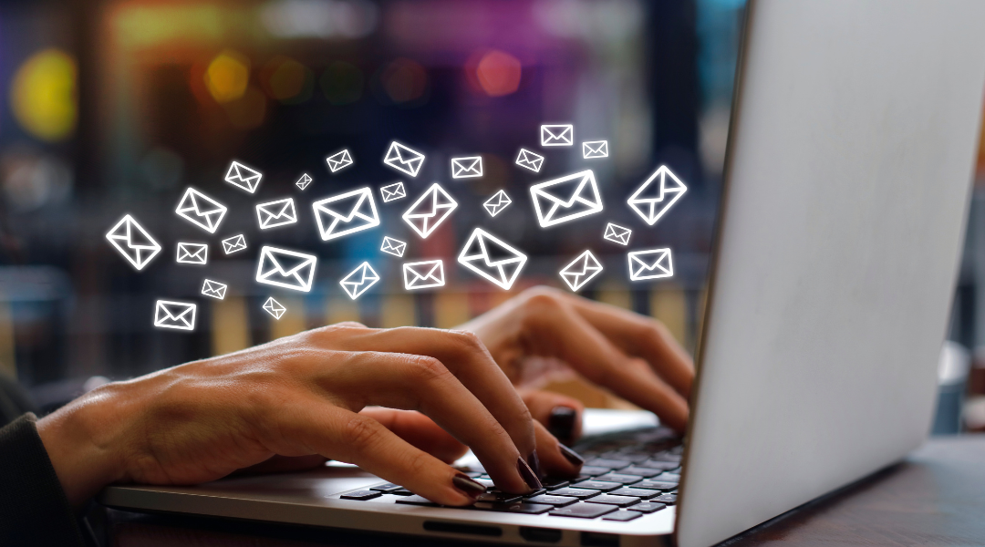 Dark manicured hands on a silver keyboard with numerous white envelope icons floating around,