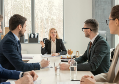 Three men and two women in business suits, talking seriously at a conference table.