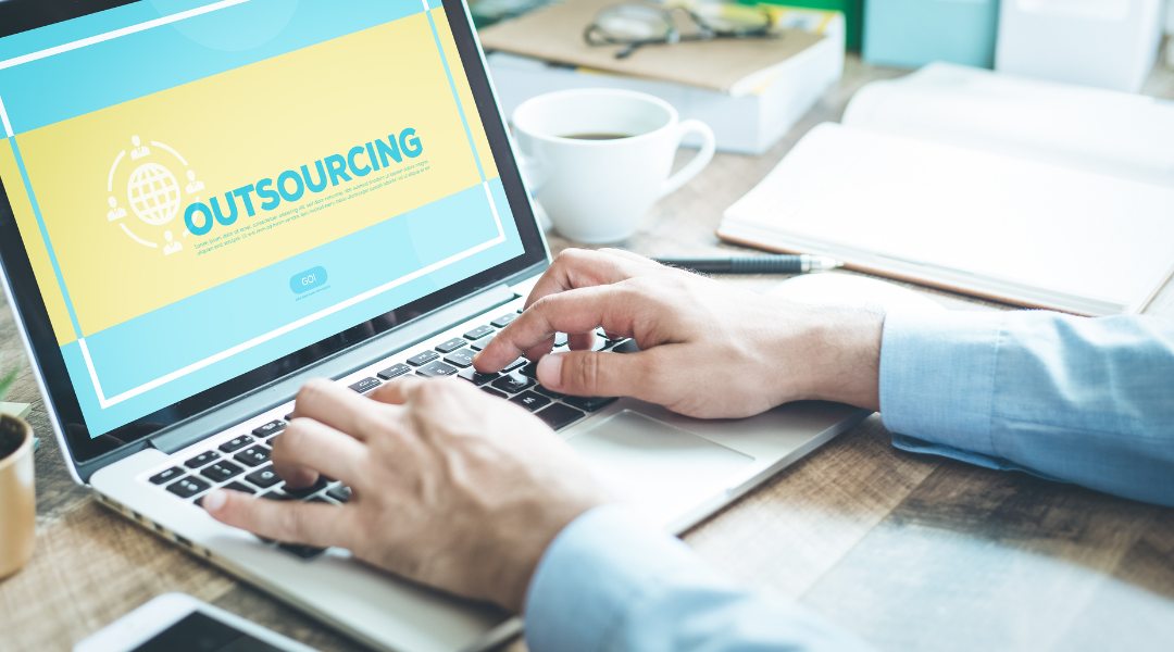 Someone working at a desk with a laptop Screen shows a blue and yellow outsourcing website.