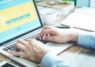 Someone working at a desk with a laptop Screen shows a blue and yellow outsourcing website.