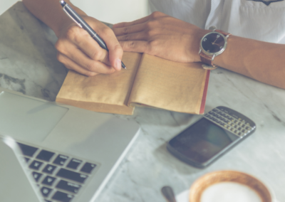 A person at a marble desktop writing in a brown notebook.