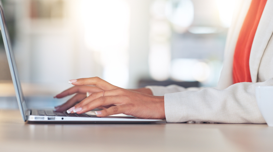 a woman in a white suit and orange top typing on a laptop.