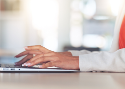 a woman in a white suit and orange top typing on a laptop.