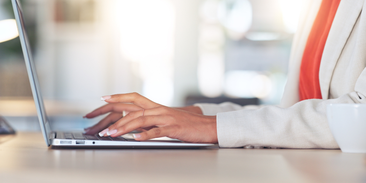 a woman in a white suit and orange top typing on a laptop.