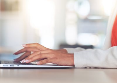 woman wearing a white blazer and orange top working at a laptop.