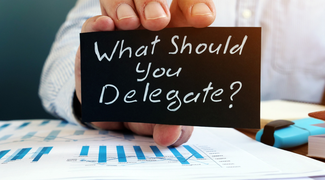 a man's hand holding a black sign with the words what should you delegate on it,