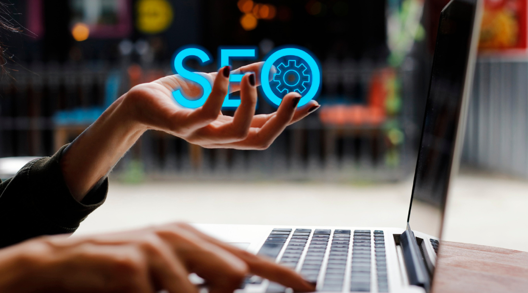 person at a laptop keyword. One hand is holding the letters SEO in its palm.