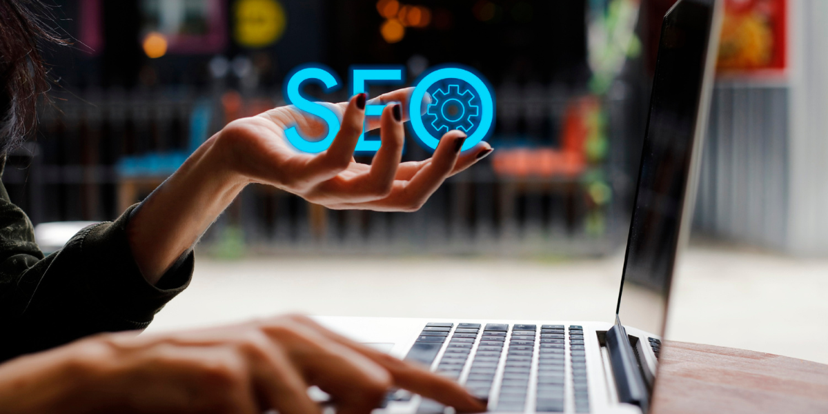 person at a laptop keyword. One hand is holding the letters SEO in its palm.