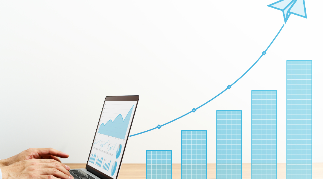 Hands typing on a laptop with graphs on the screen, including an upward bar graph and a flying paper airplane icon, indicating increasing sales.