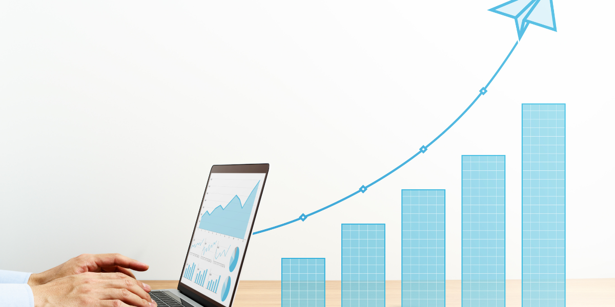 Hands typing on a laptop with graphs on the screen, including an upward bar graph and a flying paper airplane icon, indicating increasing sales.