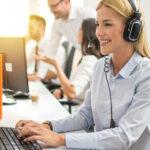Outsourced customer service professional in headset working on computer in call center 
