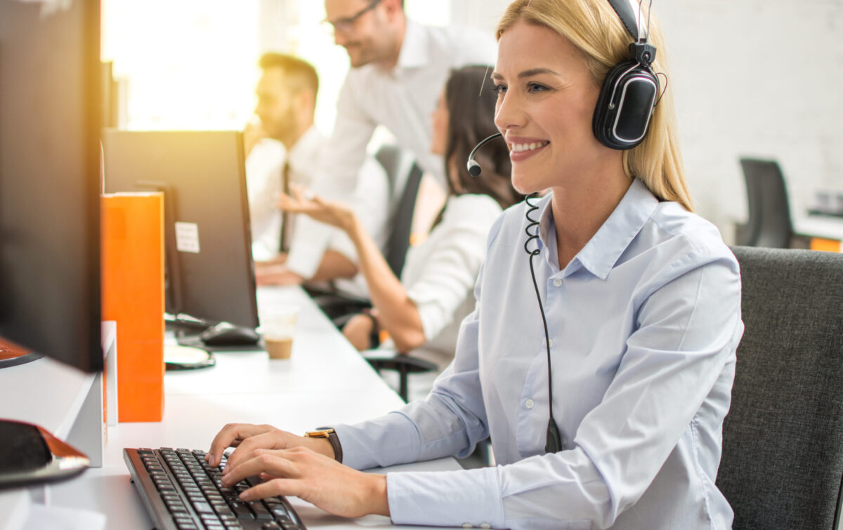 Outsourced customer service professional in headset working on computer in call center 