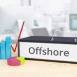 Folder on desk with offshore label beside finance diagrams.