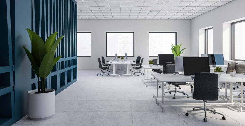 Modern office with desks, chairs, and potted plants, lit by natural light.