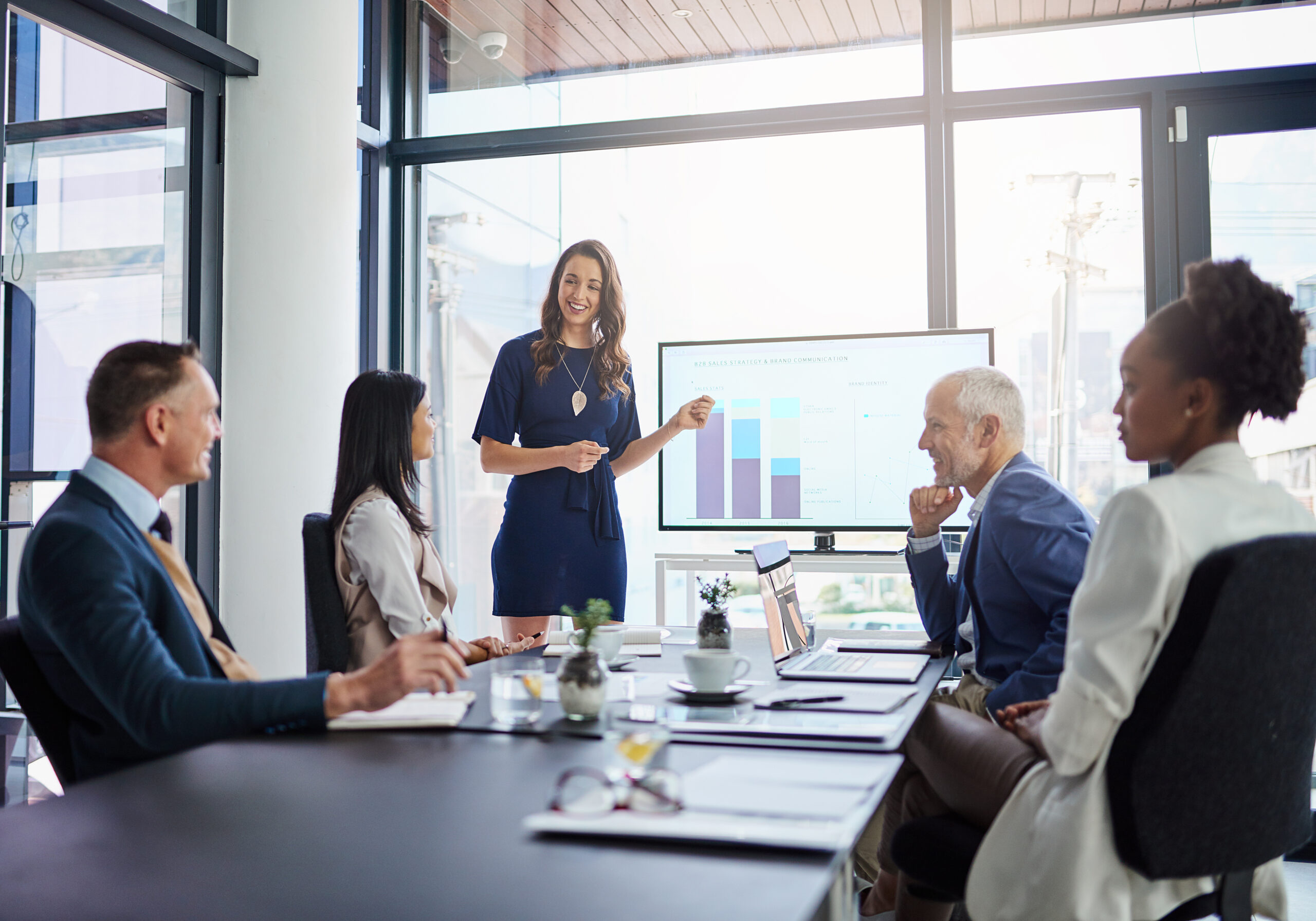 Businesswoman analysis giving a statistic presentation in a diverse boardroom. Professional business female presenting to her work colleagues in the conference room, explaining graphics for growth. Legal team watching a presenter explain how to grow a law firm while keeping costs down.