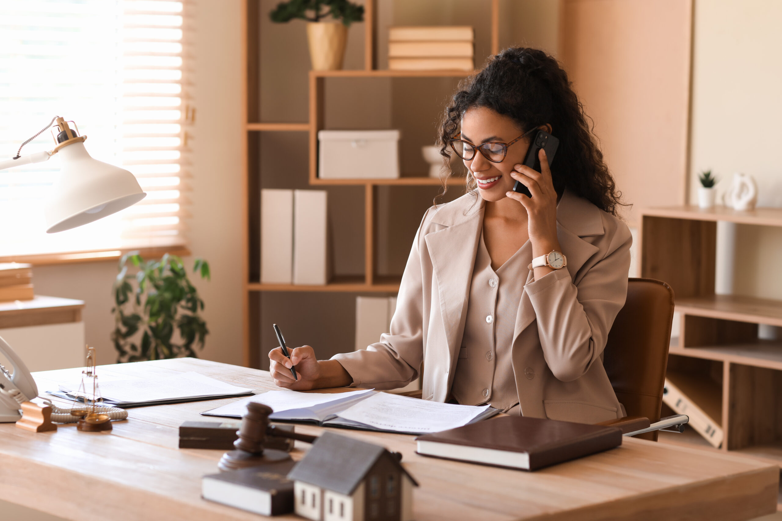 Female African-American lawyer talking by mobile phone at table in office Virtual Paralegal reviews law briefs and memos for a law firm client