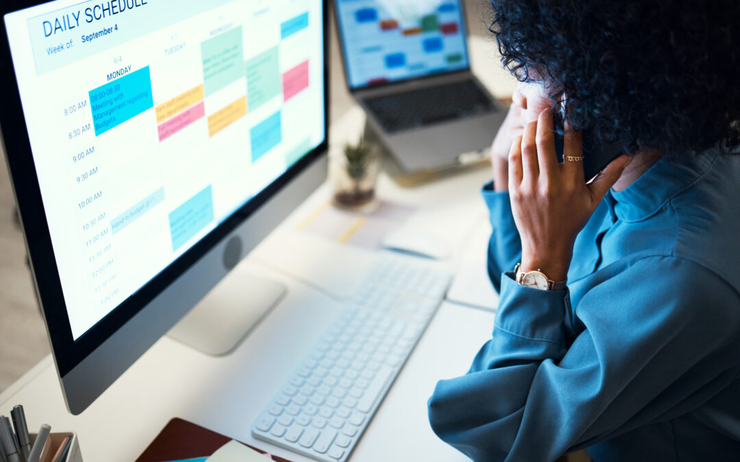 A professional woman managing client intake using a laptop, smartphone, and digital calendar at her desk.