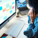 A professional woman managing client intake using a laptop, smartphone, and digital calendar at her desk.