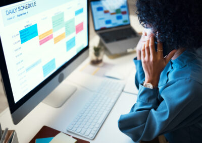 A professional woman managing client intake using a laptop, smartphone, and digital calendar at her desk.