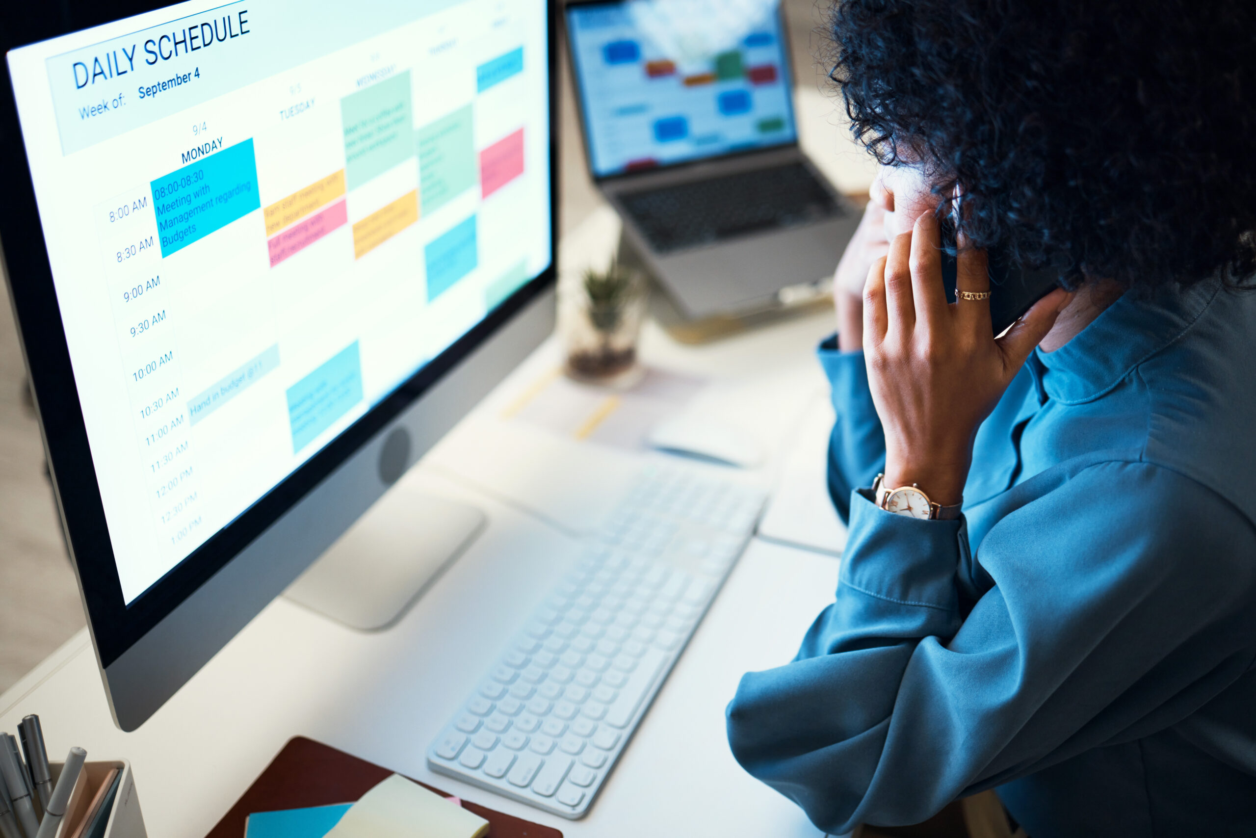 A professional woman managing client intake using a laptop, smartphone, and digital calendar at her desk.