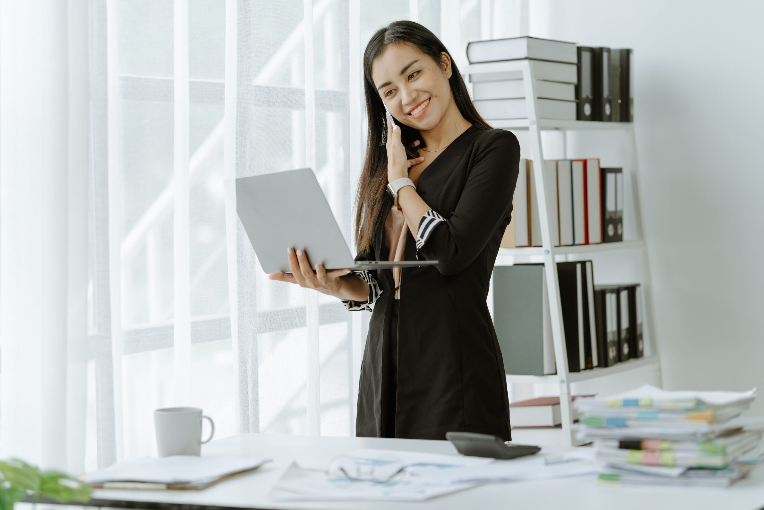 Asian woman sitting at a desk working in the office use a computer, laptop A virtual executive assistant updates her team on project updates and progress.